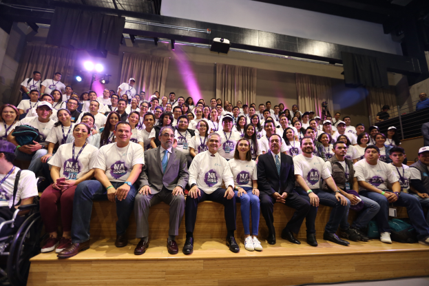 Eine Gruppe von Menschen sitzt auf einer Bühne mit einer Person im Rollstuhl links, hinter Vorhängen, Scheinwerfern und einer Wand auf der Nationalen Konferenz der Frauen-Basketball-Vereinigung.