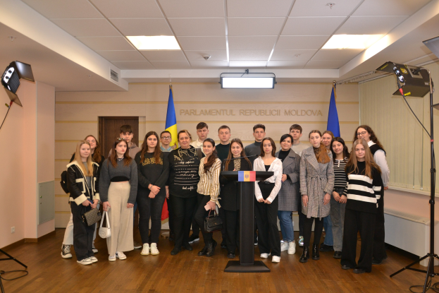 Gruppe von Menschen vor einem Podium mit Mikrofon auf dem "Moldova Youth Congress 2018"-Event, umgeben von Fahnen, einer Wand mit Text, einer Tür, einer Decke mit Deckenleuchten und Stativen.