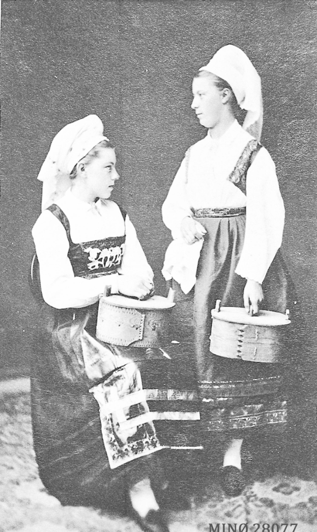 Zwei junge Frauen in traditioneller schwedischer Kleidung, die in einem Schwarz-Weiß-Foto Trommeln spielen.