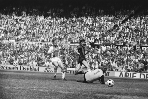 Schwarä-weßes Foto von Männern, die auf einem Feld Fussball spielen, mit Zuschauern im Hintergrund und einer Tafel mit der Aufschrift "Bundesliga 1978-79 Ajax 1-1 Hannover 96."