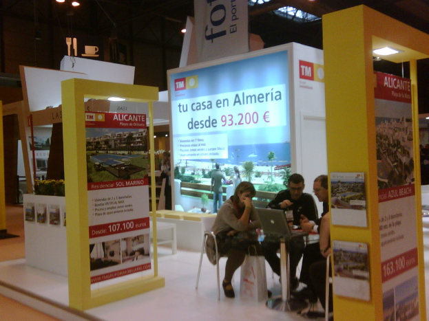 Eine Gruppe von Menschen sitzt um einen Tisch herum auf Stühlen und schaut auf einen Laptop, mit mehreren Flyern, auf denen verschiedene Anzeigen zu sehen sind.