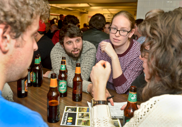 Mehrere Personen auf beiden Seiten eines Tisches mit Bierflaschen, die scheinbar in einer Bar stehen.
