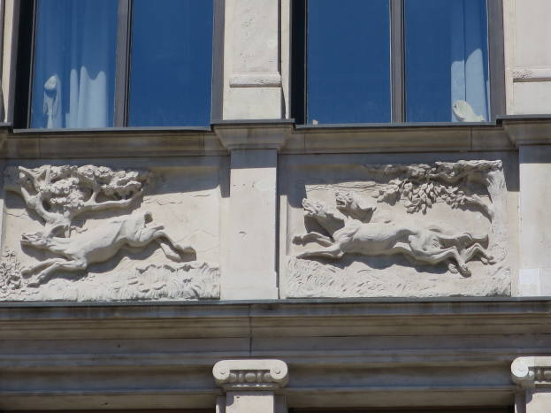 Ein Gebäude mit Glasfenstern, verzierte Ornamente an der Fassade und eine Tür unten.