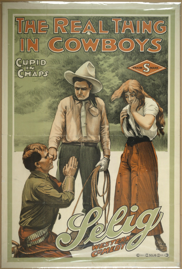 Plakat an einer Wand mit drei Personen – zwei Männer mit Cowboyhüten und eine Frau in einem langen Kleid – mit der Aufschrift "The Real Thing in Cowboys" in fetter schwarzer Schrift auf einem hellgelben Hintergrund.