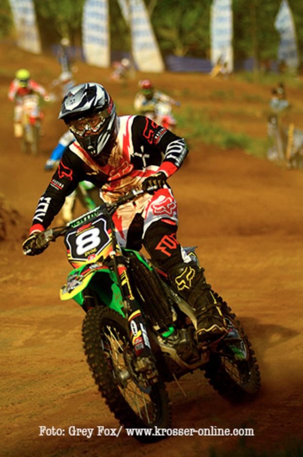 Mehrere Motorradfahrer mit Helmen auf einer Rennstrecke mit Text unten im Bild.