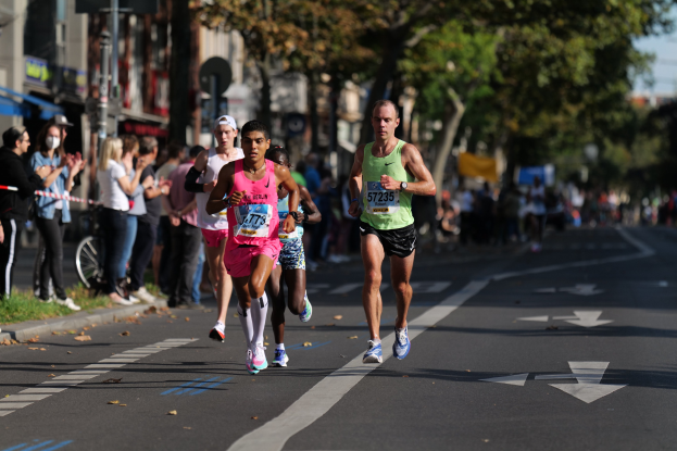 Gruppe von Menschen, die bei einem Stadtmarathon laufen, mit Zuschauern und unscharfem städtischem Hintergrund.