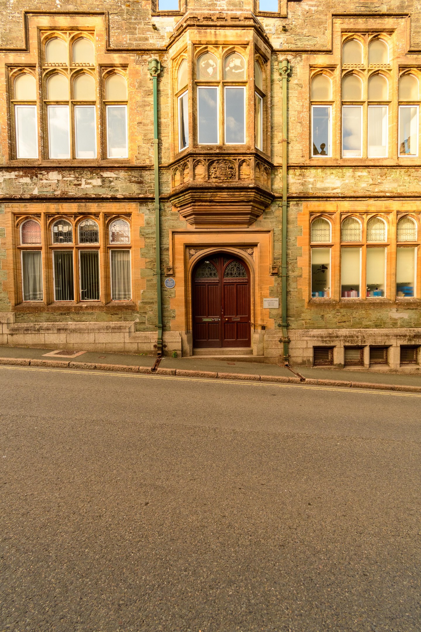 Altes Gebäude mit vielen Fenstern, einer Holztür und Rohren an den Wänden, das neben einer Straße liegt.