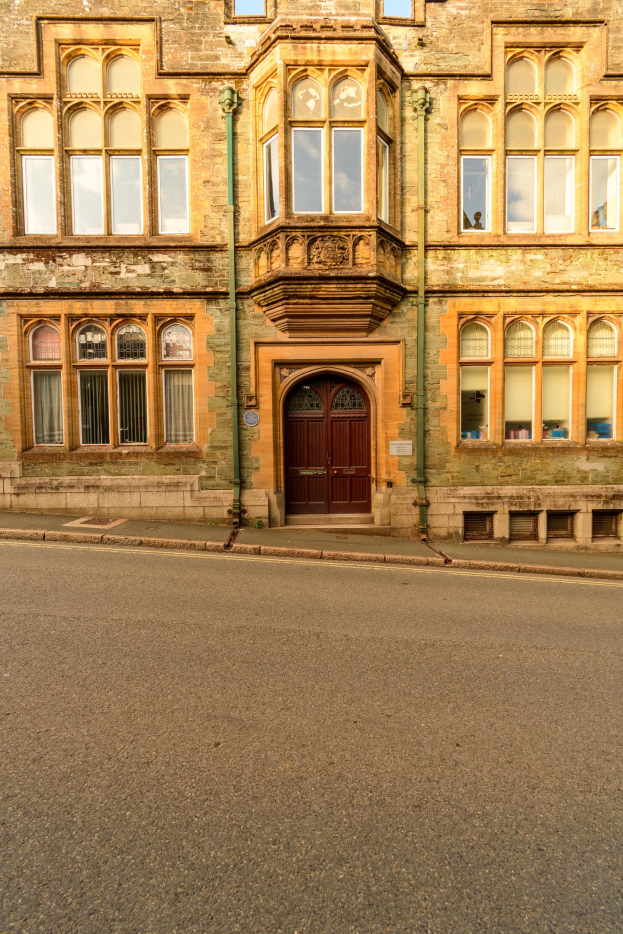 Altes Gebäude mit vielen Fenstern, einer Holztür und Rohren an den Wänden, das neben einer Straße liegt.