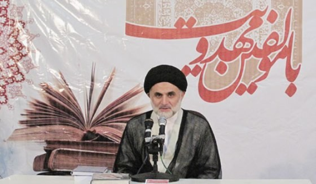 Ayatollah Ali Khamenei, der Oberste Führer von Iran, sitzt vor einem Tisch mit Büchern und Mikrofonen, mit einem Banner mit Text und einem Bild eines Buches dahinter.