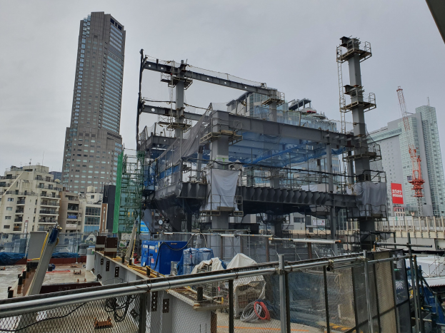 Großbaustelle in einer Stadt für ein neues Kraftwerk, umgeben von einem Metallzaun, mit Gebäuden, Polen, einer Fahne, Fahrzeugen, Drähten und einem bewölkten Himmel.