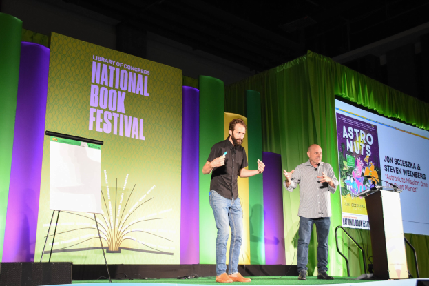 Zwei Männer auf einer Bühne mit einem Podium und einem Mikrofon rechts daneben.