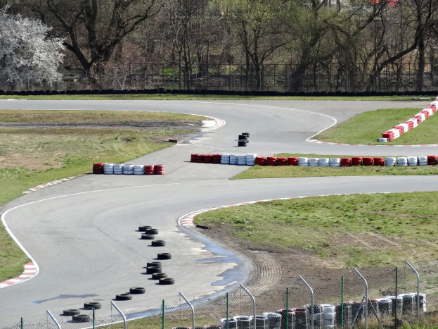 Rennstrecke mit zahlreichen Reifen entlang ihrer Ränder, umgeben von Gras und Maschendrahtzaun, mit im Hintergrund sichtbaren Bäumen.