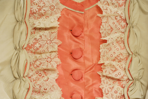 Nahaufnahme eines rosafarbenen und cremefarbenen Kleides mit weißer Spitze und vorderen Knöpfen.