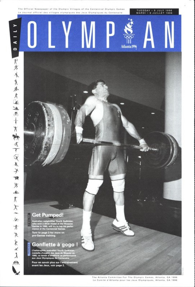 Schwarzes und weißes Foto eines Mannes in einem Gewichtheber-Outfit, der eine Hantel mit entschlossener Miene stemmt, mit dem Text "Olympian Magazine" oben.