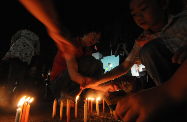 Mehrere Personen zünden Kerzen am Bildunterrand an.