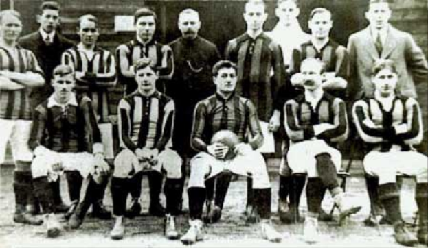 Ein Schwarz-Weiß-Foto einer Fußballmannschaft, mit einigen stehenden und einigen sitzenden Spielern vor einer Wand, mit dem Text 'Ballymena Football Club' unten.