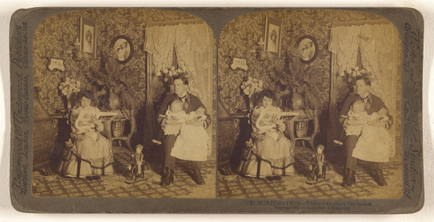 Ein altes Familienfoto, das einen Mann und eine Frau zeigt, die in der Mitte sitzen und jeweils ein Baby halten, umgeben von Blumentöpfen, Vorhängen und Fotorahmen an der Wand.