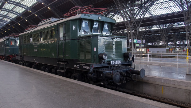 Ein Zug auf Schienen mit Geländern und Planken im Hintergrund, Lampen auf dem Dach und Himmel darüber, mit einem Boden darunter.