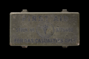 Metallischer Verbandkasten mit der Aufschrift "Verbandkasten für Gasopfer" vor schwarzem Hintergrund.