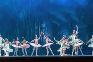 Eine Gruppe von Balletttänzern in bunten Kostümen führt synchronisierte Bewegungen auf der Bühne mit einem blauen Hintergrund während einer Aufführung von *Der Nussknacker* im Royal Opera House aus.