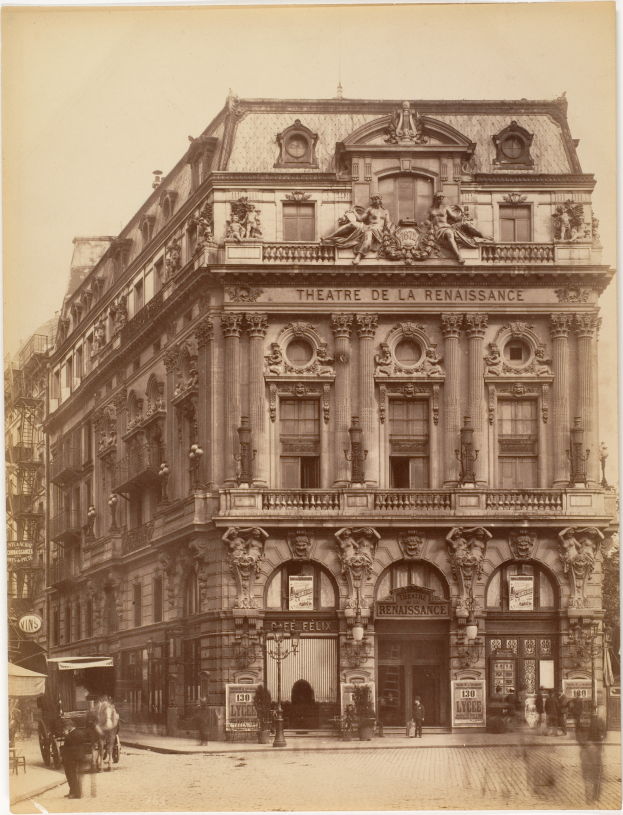 Ein altes Foto des Théâtre de la Renaissance in Paris, Frankreich, zeigt ein Gebäude mit Fenstern, Säulen, Bögen und Skulpturen an der Fassade, mit einigen Menschen und Fahrzeugen auf der Straße davor und dem Himmel im Hintergrund.