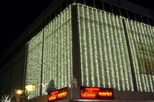 Ein festlich geschmücktes Gebäude in Berlin, Deutschland, mit Weihnachtslichtern umgeben von Bäumen, Laternenmasten und Schildern mit Text unter einem sichtbaren Himmel.