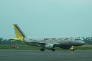 Ein Airbus A320-200 der Germanwings auf dem Rollfeld am Frankfurter Airport, mit einem Fahrzeug auf der linken Seite, Gras, Bäumen und dem Himmel im Hintergrund.