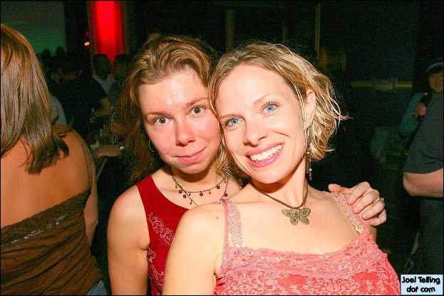 Eine Gruppe von Menschen mit zwei lachenden Frauen in der Mitte und einem Licht im Hintergrund.