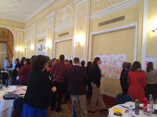 Eine Gruppe von Menschen, die Plakate und Diagramme auf einer Wand in einem Gebäude betrachten, das wie ein Kunstmuseum aussieht.