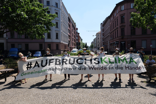 Gruppe von Menschen mit Masken, die ein Banner mit der Aufschrift 'Aufbruchsklima' während einer Klimaprotest in Berlin halten