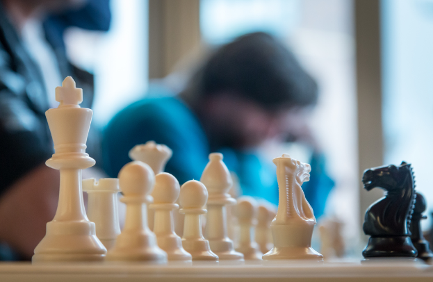 Einige Schachfiguren befinden sich auf einer Oberfläche mit einigen Personen im Hintergrund.