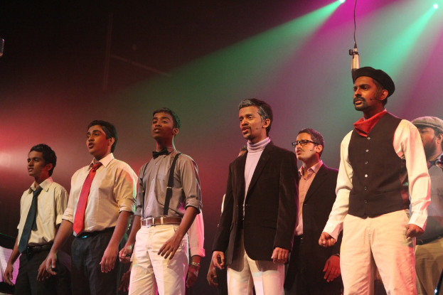 Eine Gruppe von Männern steht auf einer Bühne und führt ein Drama auf.