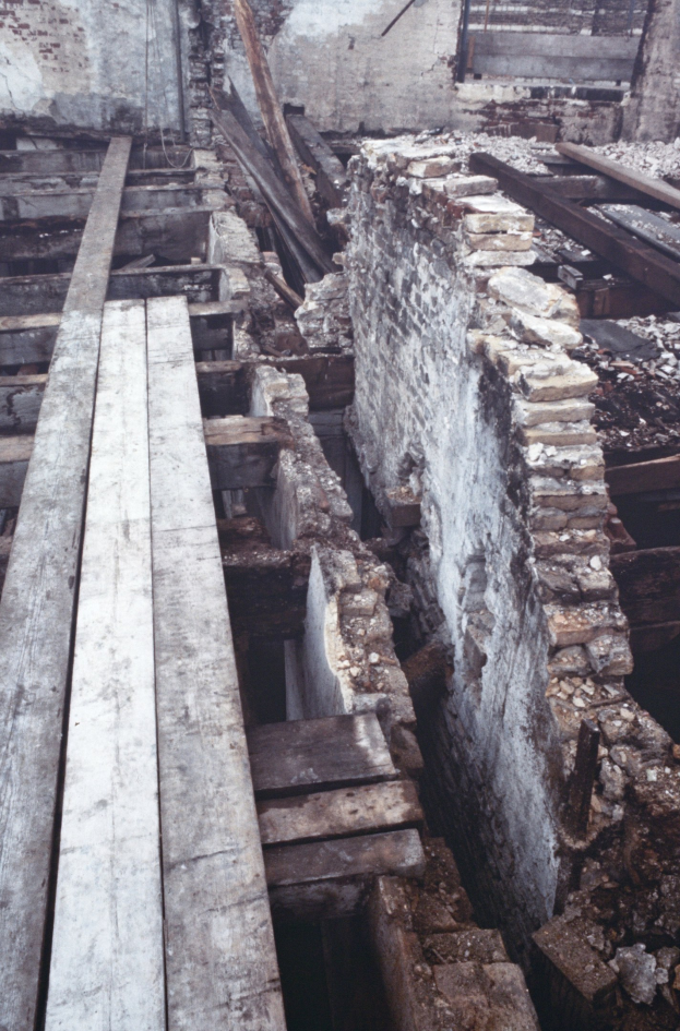 Altbau wird abgerissen mit verstreuten Holzplanken und Steinen im Vordergrund und einer verbliebenen Wand im Hintergrund.