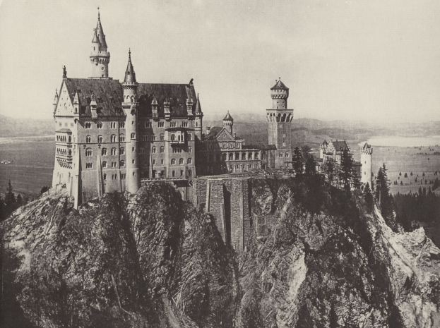 Neuschwanstein Burg in Deutschland, thront auf einem Berg umgeben von Bäumen und einem klaren Himmel, dargestellt in Schwarzweiß.