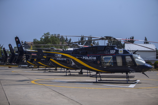 Polizeihubschrauber auf einem Flughafenvorfeld mit umgebenen Gebäuden, Bäumen und einem klaren blauen Himmel.