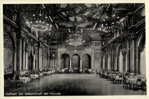Schwarzes und weißes Foto eines großen Raums mit Tischen, Stühlen, Säulen, Bögen und Kronleuchtern, beschriftet mit "Fest der Gesellschaft der Freunde, Berlin" unten.