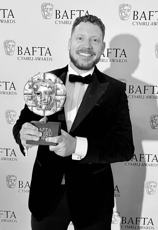 Ein Mann in einem Smoking, der eine BAFTA-Trophäe hält und lächelt, mit einem Hintergrundplakat mit der Aufschrift "BAFTA Awards 2018."
