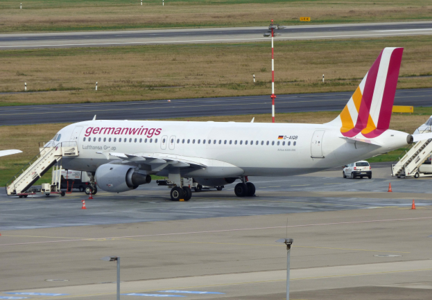 Germanwings Airbus A320-200 am Frankfurter Flughafen mit Bodenbetriebsfahrzeugen, Verkehrskegeln, Versorgungsmasten und Grünfläche im Hintergrund.