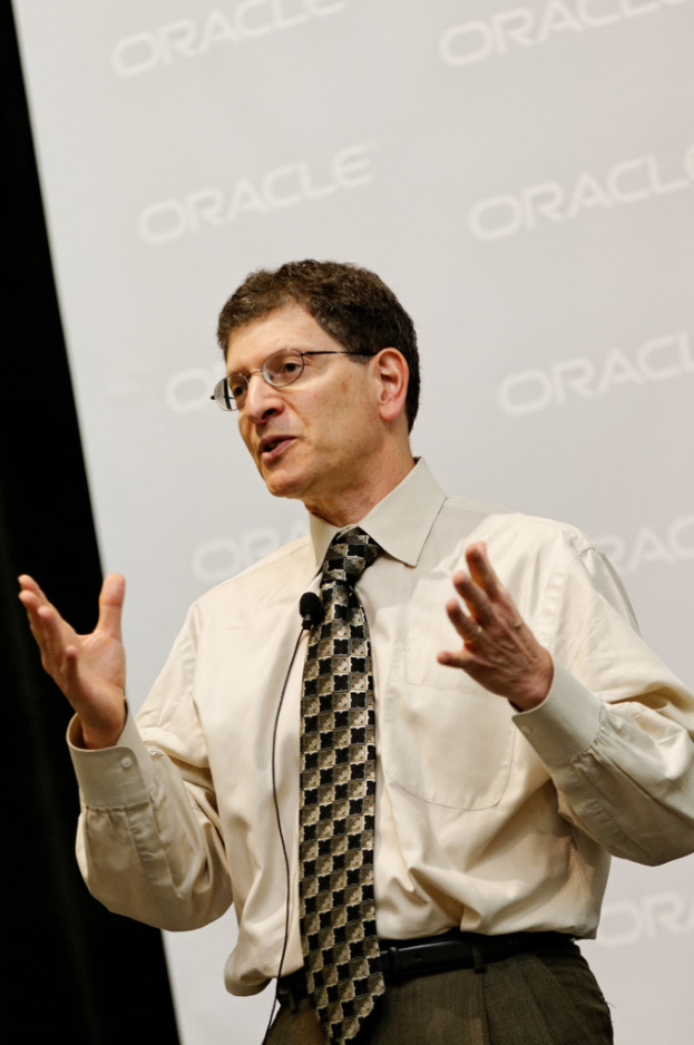 Eine Person steht vor einer Sponsorwand und tr├Ągt Kleidung und Brille.