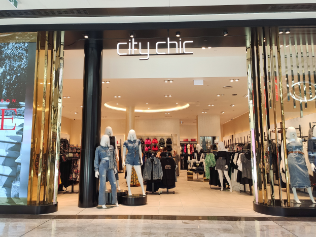 Ein stylischer Mode-Boutique in einem Einkaufszentrum mit Schaufensterpuppen in der neuesten Mode, Kleidung an Bügeln, einer Säule, einem Schild und einer gefliesten Bodenfliese.